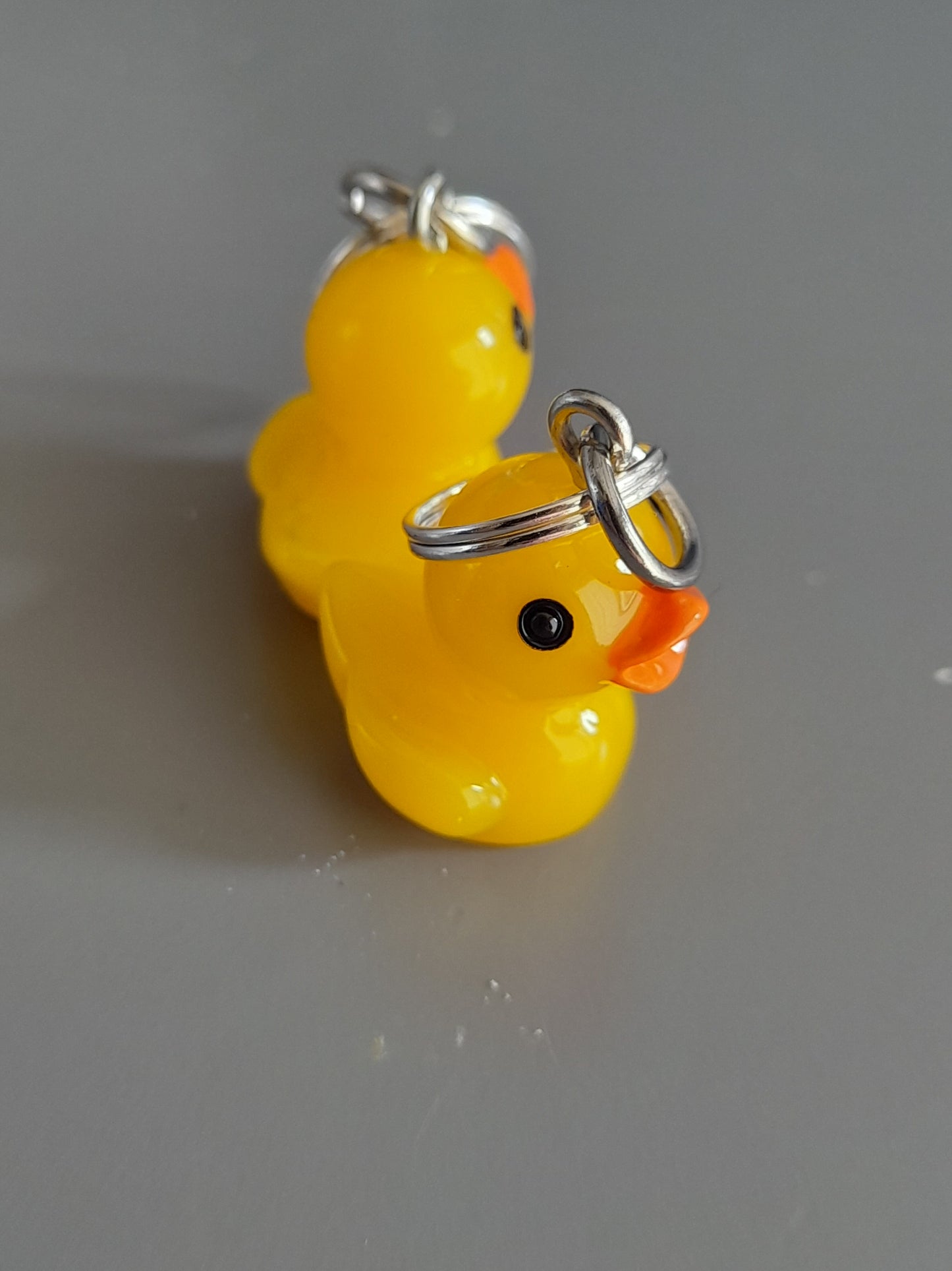 Close up of a set of 2 handmade stitch markers. They are 3D ducks with fixed ring fastenings. 